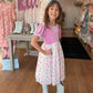 Young girl in a pink dress with floral pattern and white boots standing in a store.