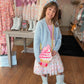 Young girl in a store wearing a light blue cardigan, pink dress, and white boots with a colorful ice cream-themed bag.
