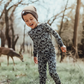 Child in camouflage outfit standing in a forest with deer in the background