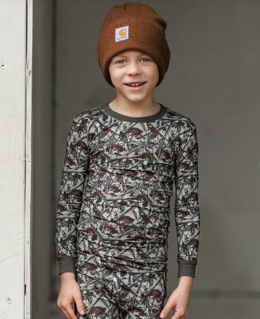 Child wearing a camouflage long-sleeve shirt and pants with a brown beanie, standing against a neutral background.