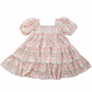 Puff sleeve dress on white background, dress has a block print reminiscent of quilting with faint watercolor looking pink hearts in the center on some blocks, and a floral print in other blocks. The skirt of the dress is sewn into three separate tiers, and the waist is in the empire style with a square neckline. 