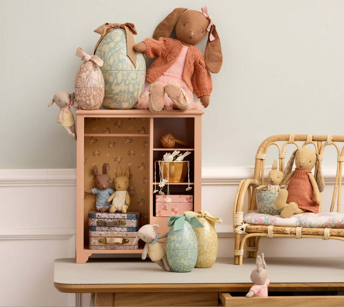 Collection of plush toys including rabbits and eggs on a shelf and chair against a light wall.