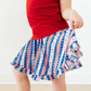 Person wearing a red top and a blue, white, and red patterned skirt on a plain background