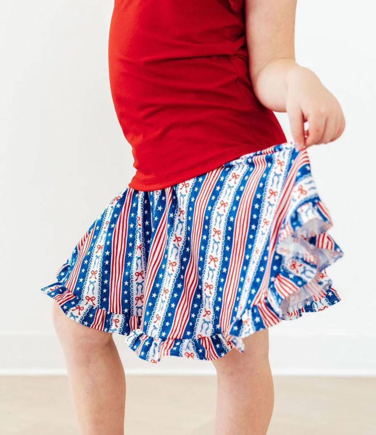 Person wearing a red top and a blue, white, and red patterned skirt on a plain background