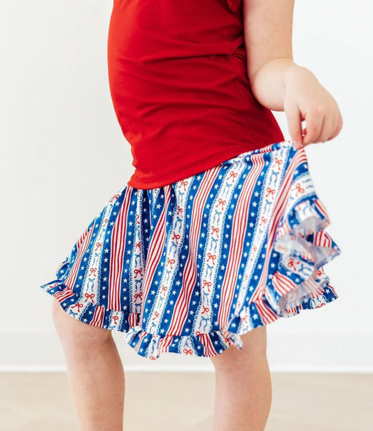 Person wearing a red top and a blue, white, and red patterned skirt on a plain background