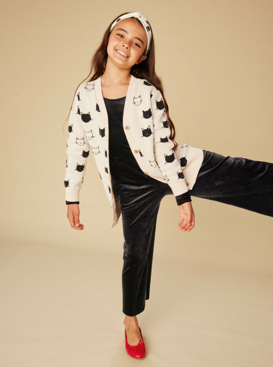 Young girl wearing a patterned cardigan and black pants on a beige background
