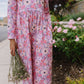 Person wearing a pink floral dress standing outdoors with flowers and greenery.