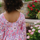Child wearing a floral dress standing in front of garden flowers