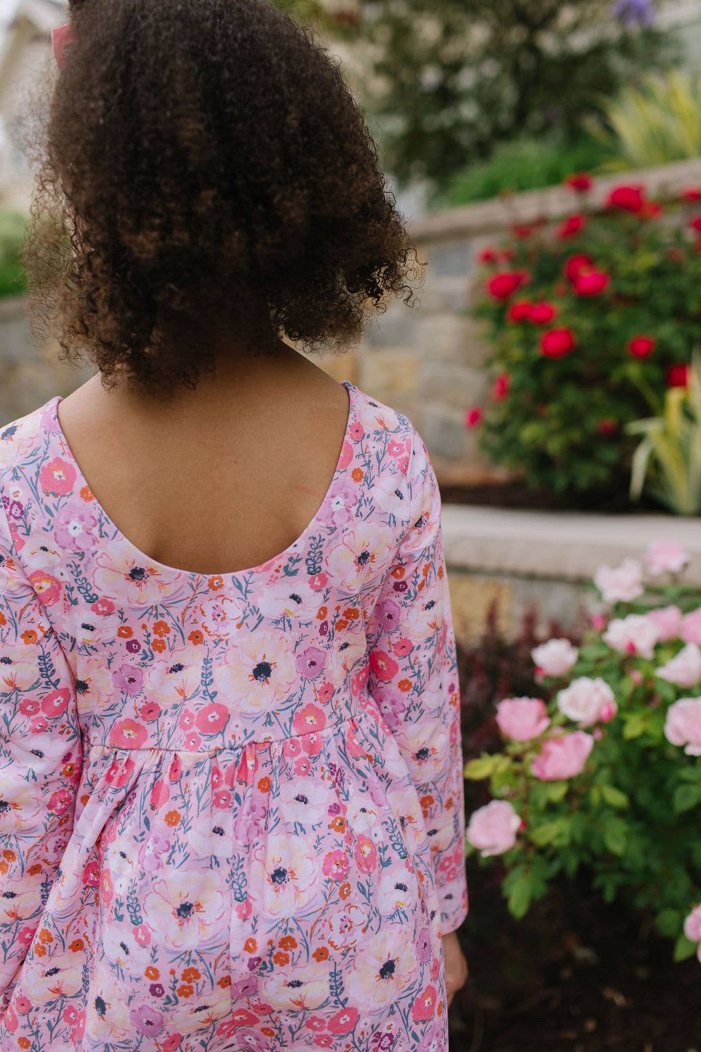 Child wearing a floral dress standing in front of garden flowers