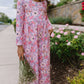 Child in a floral dress standing outdoors next to a garden.