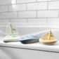 Three colorful toy boats on a white surface with a tiled wall background