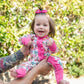 Baby in a colorful outfit being held outdoors with greenery in the background
