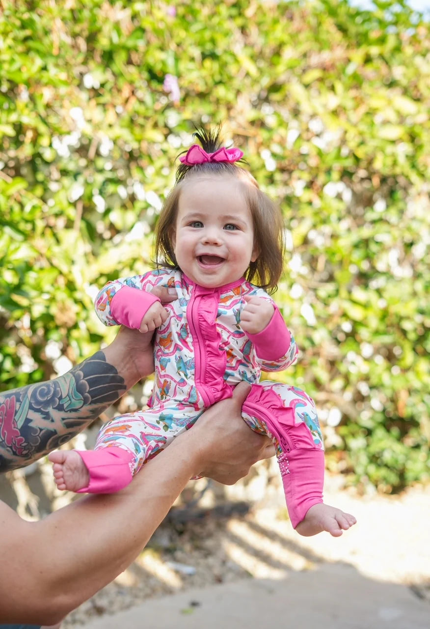 Baby in a colorful outfit being held outdoors with greenery in the background