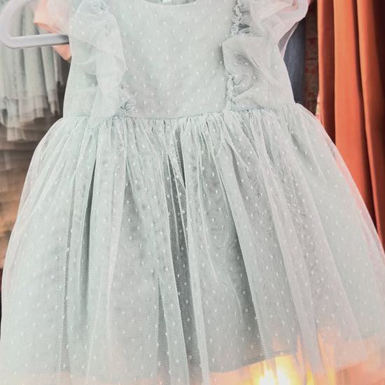 light green dress being held in front of rack with soft yellow lighting