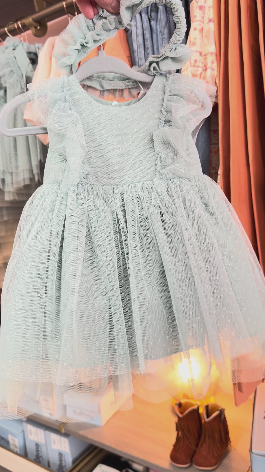 light green dress being held in front of rack with soft yellow lighting